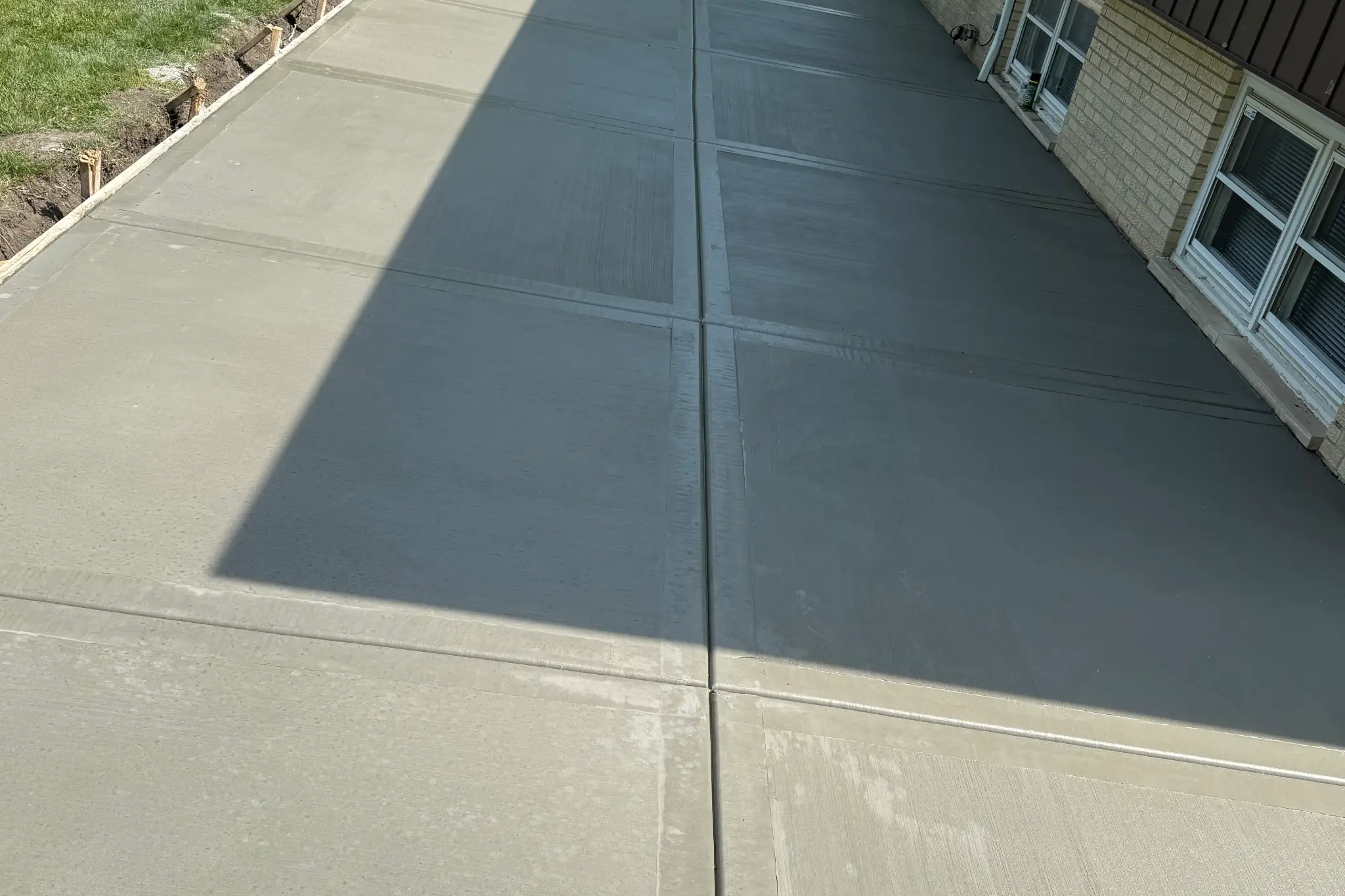 Freshly poured concrete patio with smooth surfaces, bordered by wooden forms and greenery, beside a house Freshly poured concrete patio with smooth surfaces, bordered by wooden forms and greenery, beside a house