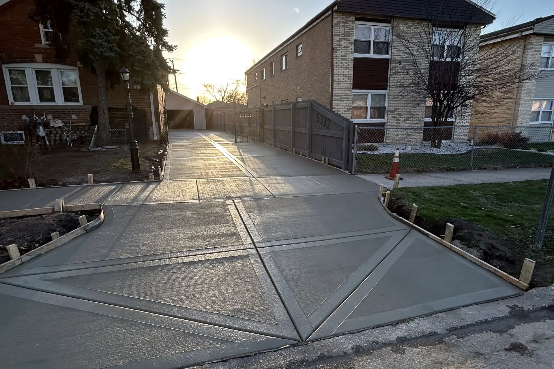 Newly poured concrete driveway with geometric patterns, flanked by a residential building and a tree at sunset Newly poured concrete driveway with geometric patterns, flanked by a residential building and a tree at sunset