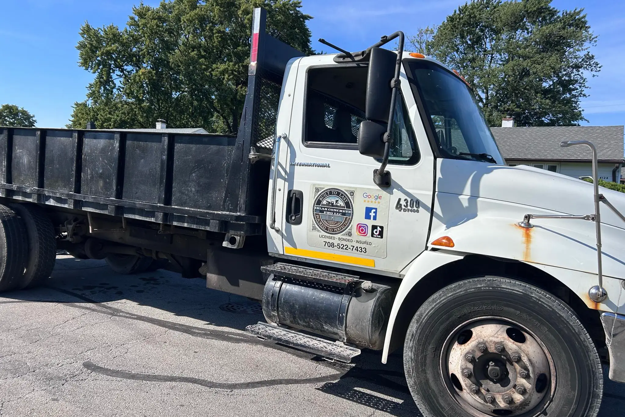 A white dump truck parked on the street, featuring a company logo and contact details on the side, under a clear blue sky A white dump truck parked on the street, featuring a company logo and contact details on the side, under a clear blue sky